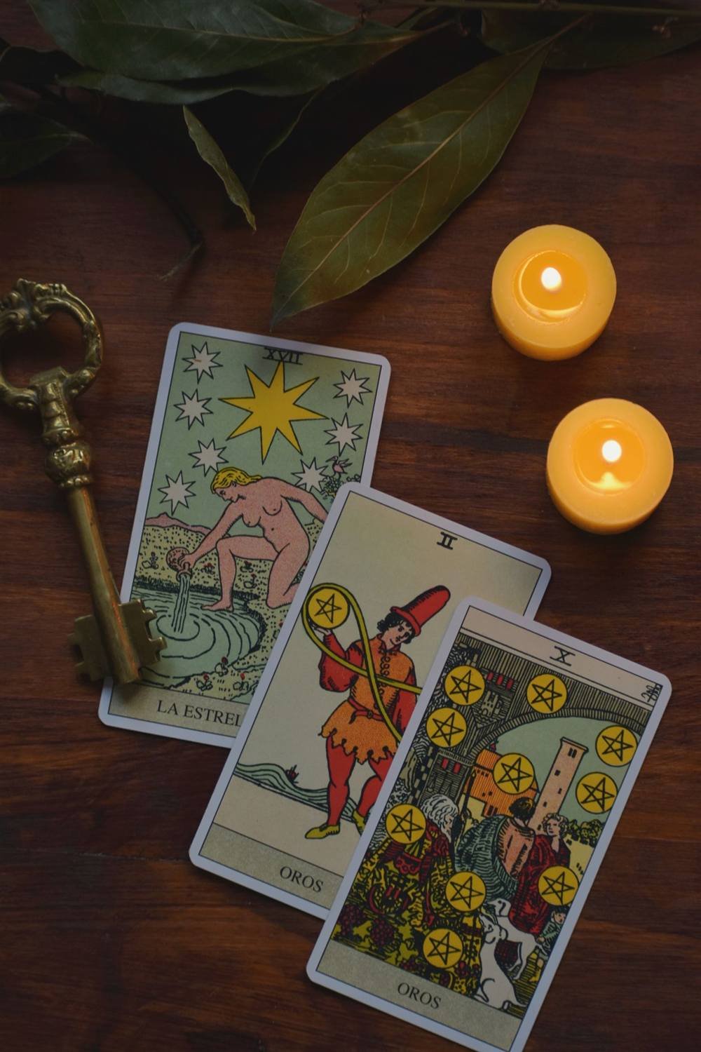 Cartas de tarot extendidas con una llave antigua y velas sobre madera