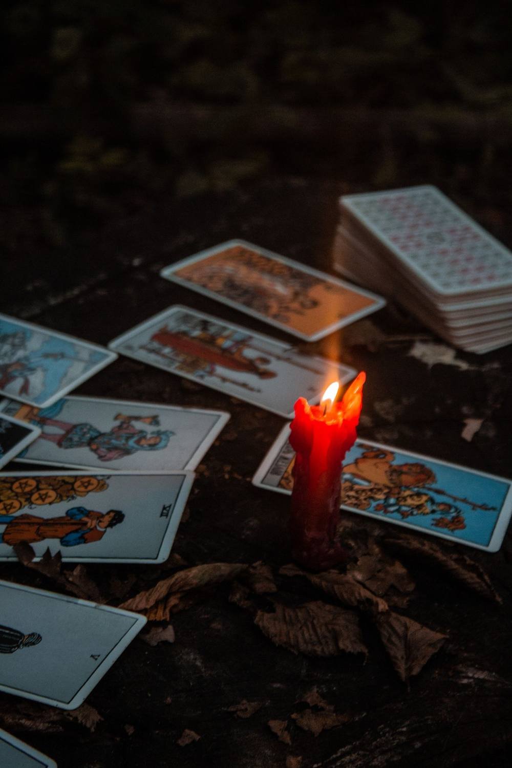 Vela roja encendida rodeada de cartas de tarot en la oscuridad